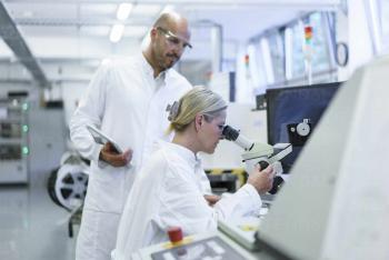 male-technician-standing-by-female-scientist-looking-into-microscope-while-doing-research-in-laboratory-MOEF03390.jpg